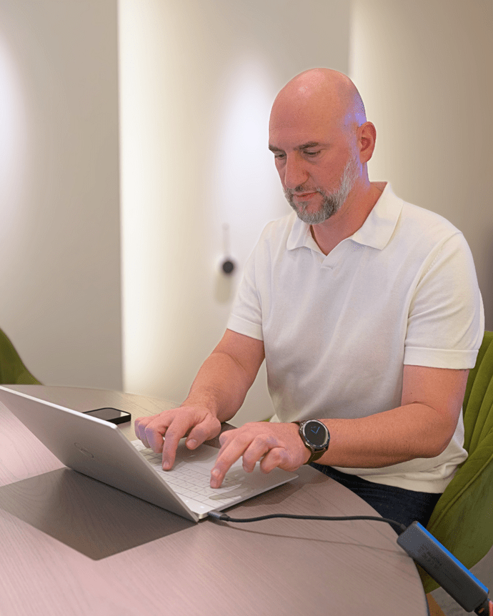 Ein Mann tippt auf einem Laptop an einem Tisch in einem modern gestalteten Raum.