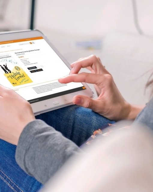 Person liest auf einem Tablet eine Buchrezension, während sie entspannt auf einem Sofa sitzt.