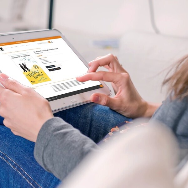 Person liest auf einem Tablet eine Buchrezension, während sie entspannt auf einem Sofa sitzt.